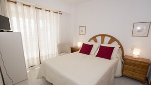 A neatly arranged hotel room with a bed, bedside tables, a chair, a television, and a refrigerator. - A102 CALPPLACE 2-5º-2 (Calpe)