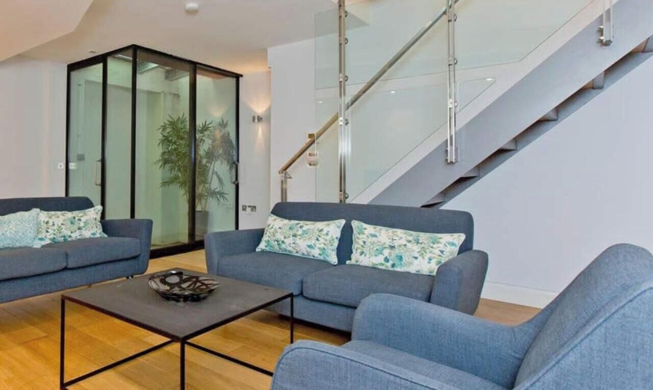 A modern living room with two sofas, a coffee table, and a staircase with glass railings.