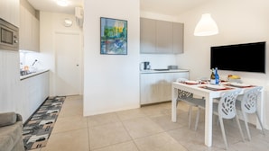 A modern kitchen with a dining area, white cabinetry, a painting on the wall, and a flat-screen TV mounted above the table. - Holiday Apartment "Casa Punta Grò" with Shared Pool, Terrace and Wi-Fi (Sirmione)