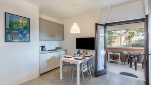 A modern kitchen with white cabinets, a dining table with chairs, a TV mounted on the wall, and a balcony with outdoor seating. - Holiday Apartment "Casa Punta Grò" with Shared Pool, Terrace and Wi-Fi (Sirmione)