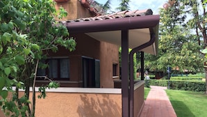 A building with a covered patio area, a window with shutters, and a pathway leading to a green lawn. - Holiday Apartment "Casa Punta Grò" with Shared Pool, Terrace and Wi-Fi (Sirmione)