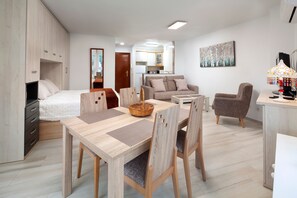 A modern, well-lit living room with a dining area, a kitchenette, and a bedroom.