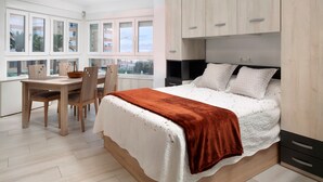 Quarto com cama, escrivaninha, cadeiras e janela com vista.