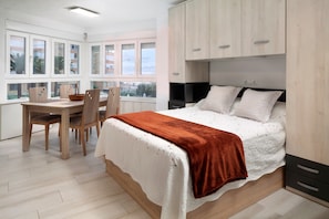 A bedroom with a bed, a desk with chairs, and a window with a view.