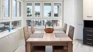 Cozinha moderna com mesa de jantar, cadeiras, cesta de vime e janelas amplas com vista para palmeiras.
