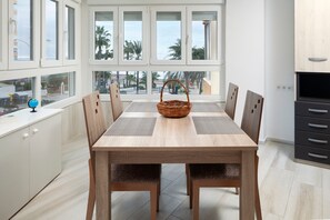 A modern kitchen with a dining table, chairs, a wicker basket, and large windows with a view of palm trees.