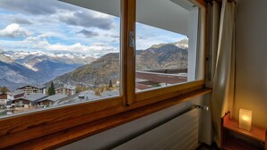 A room with a large window overlooking a mountainous landscape, a wooden shelf, and a lit candle. - Appartement Mont Parrain 14 - La Tzoumaz, 4 Vallees (La Tzoumaz)
