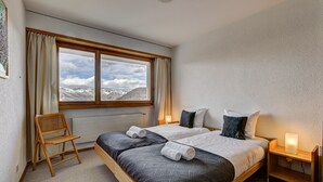 A bedroom with a large window, a wooden bed, a bedside table with a lamp, and a chair. - Appartement Mont Parrain 14 - La Tzoumaz, 4 Vallees (La Tzoumaz)