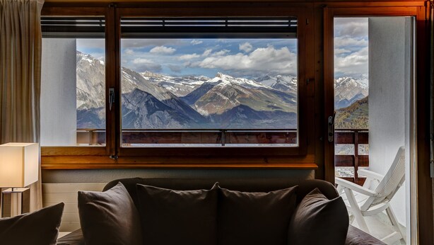 A room with a large window offering a mountain view, a wooden ceiling, and a white chair by the window. - Appartement Mont Parrain 14 - La Tzoumaz, 4 Vallees (La Tzoumaz)