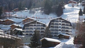 A snow-covered resort with multiple chalet-style buildings, ski lifts, and a forested backdrop. - Appartement Mont Parrain 14 - La Tzoumaz, 4 Vallees (La Tzoumaz)
