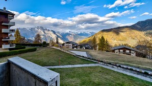 A residential area with a view of snow-capped mountains, a grassy hill, and a modern building with a balcony. - Appartement LaForet 23 - La Tzoumaz, 4 Vallees (La Tzoumaz)