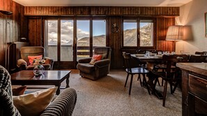 A cozy room with wooden walls, a dining area, and large windows offering mountain views. - Appartement LaForet 23 - La Tzoumaz, 4 Vallees (La Tzoumaz)