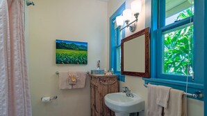 A bathroom with a wooden vanity, a white sink, a mirror, and a window with a view of greenery.