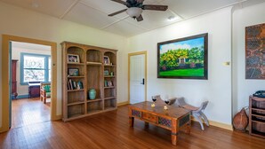 A spacious room with hardwood floors, a wooden bookshelf, a dining table with chairs, a ceiling fan, and a large framed painting.