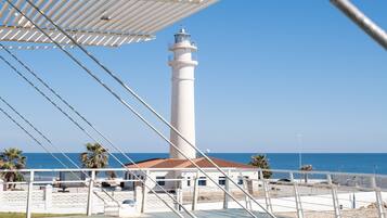 A lighthouse with a white tower and red roof, a white building with a red roof, and a clear blue sky.