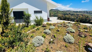 A modern white building with a sloped roof, a small porch, and a view of a hilly landscape. - Holiday Home "Villa Camacho xxvii" with Sea View, Pool & Wi-Fi (Arco da Calheta)