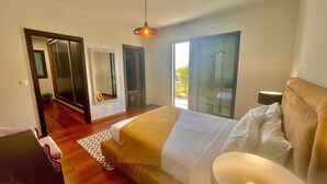 A hotel room with a bed, a desk, a chair, a large mirror, and a view of the outdoors. - Holiday Home "Villa Camacho xxvii" with Sea View, Pool & Wi-Fi (Arco da Calheta)