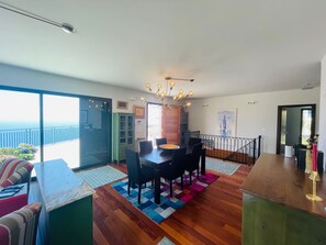 A modern living room with a dining area, large windows, and a view of the ocean.