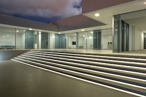 A modern building with glass doors, a staircase with illuminated steps, and a recessed ceiling.