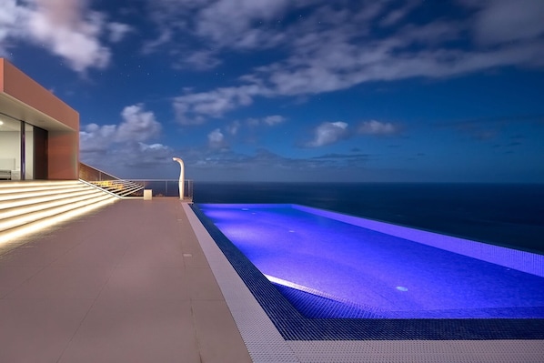 A pool with a view of the ocean, a staircase, and a modern building.