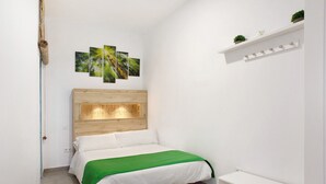 A bedroom with a wooden headboard, a green bedspread, a white wall, a shelf with plants, and a door. - Vacation 'Jardin Cardona' with Wi-Fi (Arucas)