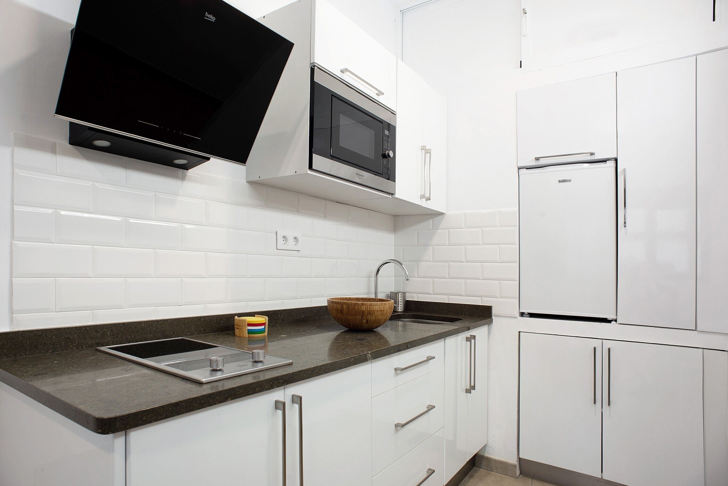 A kitchen with white cabinets, a black microwave, a stainless steel refrigerator, and a wooden bowl on the countertop.