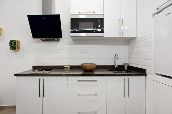 A modern kitchen with white cabinets, a microwave, a sink, and a flat-screen TV mounted above the counter.