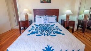 Un lit bien fait, recouvert d’une couvre-lit à motifs floraux, deux tables de chevet avec des lampes, une tête de lit en bois et un tableau accroché au mur.