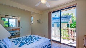Une chambre avec un lit, un ventilateur de plafond, une fenêtre et une porte-fenêtre coulissante donnant sur un espace extérieur avec vue sur la verdure.