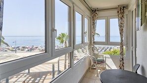 A balcony with a view of the beach, a table, and chairs.