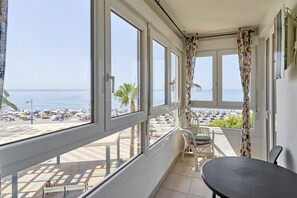 A balcony with a view of the beach, a table, and chairs.