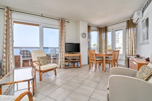 A living room with a TV, dining table, chairs, and a balcony with curtains.