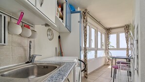 A kitchen with a sink, a clock, and a window with curtains.