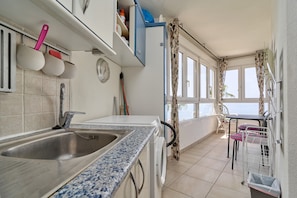 A kitchen with a sink, a clock, and a window with curtains.