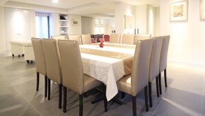 Een eetgedeelte met een grote tafel, meerdere stoelen en een bank op de achtergrond.
