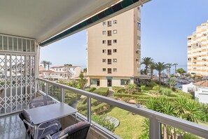 A balcony with a table and chairs, overlooking a courtyard with palm trees and a building with multiple windows. - Apartment "Familiar Torrox A65" with Sea View, Private Terrace and Wi-Fi (Torrox)
