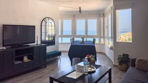 A living room with a TV, a dining table, and a view of the sea. - Apartment "Vistas Playa Torrox A73" with Sea View, Shared Pool and Wi-Fi (Torrox)