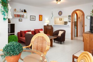 A living room with a sofa, chairs, a table, a bookshelf, and a kitchen area visible through an archway. - Apartment "Junto a la Playa A11" with Sea View, Shared Pool & Wi-Fi (Torrox)