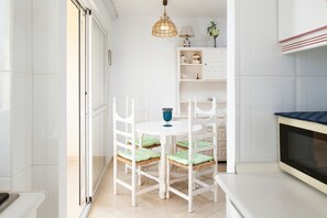 A kitchen with white cabinetry, a microwave, a dining table with chairs, and a hanging light fixture.