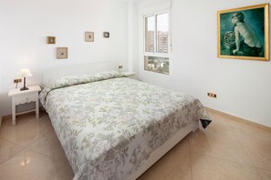 Une chambre à coucher avec un lit, une table de chevet, une lampe, une fenêtre et un tableau au mur.