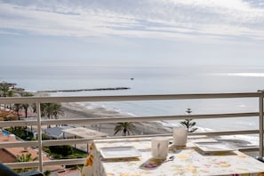 A balcony with a table set for two, overlooking a beach and ocean.