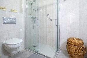 Une salle de bain avec une douche à parois de verre, des toilettes blanches et un panier en osier.