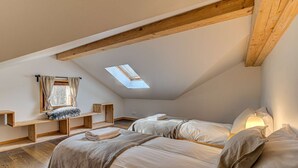Un dormitorio acogedor en el ático con dos camas, vigas de madera, un tragaluz y una ventana con cortinas.