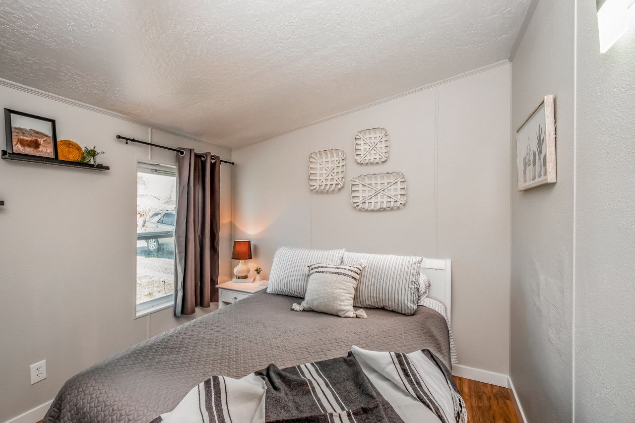 Une chambre à coucher comprenant un lit, une table de chevet, une lampe, une fenêtre avec des rideaux et des œuvres d’art murales.