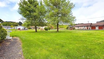A residential area with a large grassy lawn, a tree, and houses in the background.
