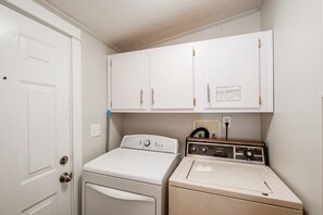 A laundry room with a front-loading washer and a top-loading dryer, white cabinets above, and a door to the left.