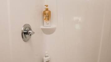 Un baño con ducha, grifo y tres repisas con artículos de tocador.