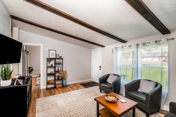 A spacious living room with a wooden ceiling, a black leather sofa, a wooden coffee table, and a bookshelf.
