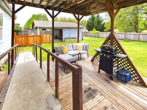 Une terrasse couverte avec un barbecue, du mobilier d’extérieur et une clôture en bois en arrière-plan.