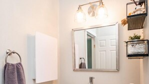 A bathroom with a white sink, a mirror, and a towel rack. There are two baskets under the sink, one containing towels and the other containing toilet paper. - Escape to a beautiful country getaway (Philomath)